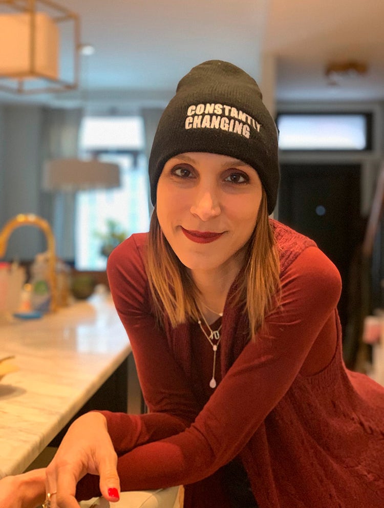 Monica Berg leans on kitchen counter while wearing a beanie that says "constantly changing"