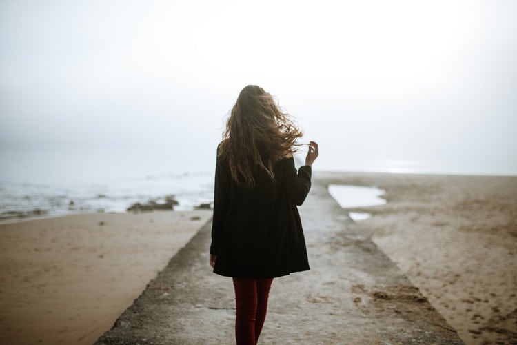 A woman with long brown hair walks down a beach boardwalk on a grey day