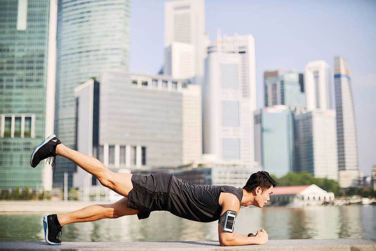 man doing one-leg plank while working out in front of a city with buildings