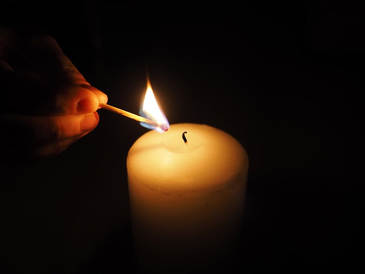 Closeup of a hand lighting a candle with a match in a dark room