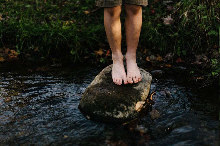 Bare feet standing on a small rock in a creek