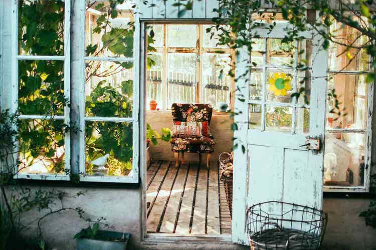 A sunny porch filled with plants and a floral-patterned chair