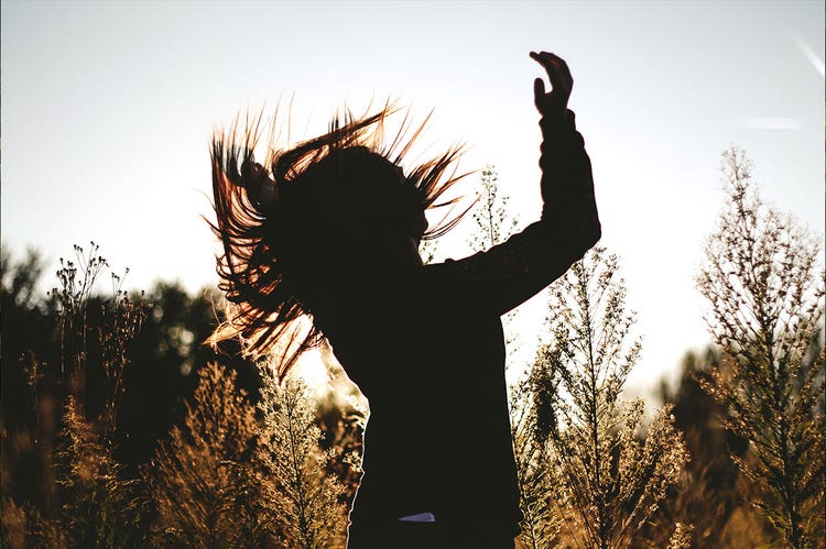 A silhouetted person twirls in a grassy field
