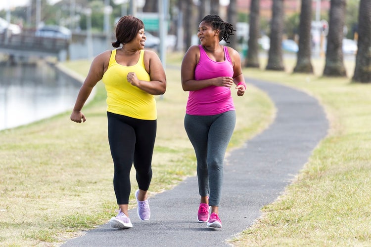 Two women in pink and yellow tank tops running in a park